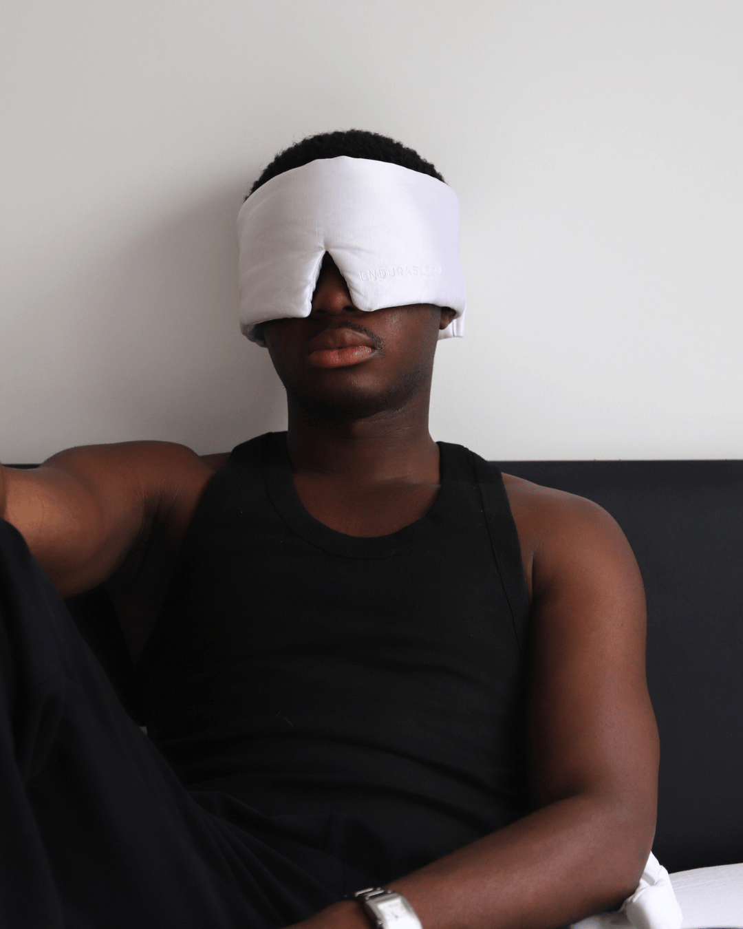 Man wearing the EnduraSleep hemp and silk sleep mask in white while relaxing on a couch