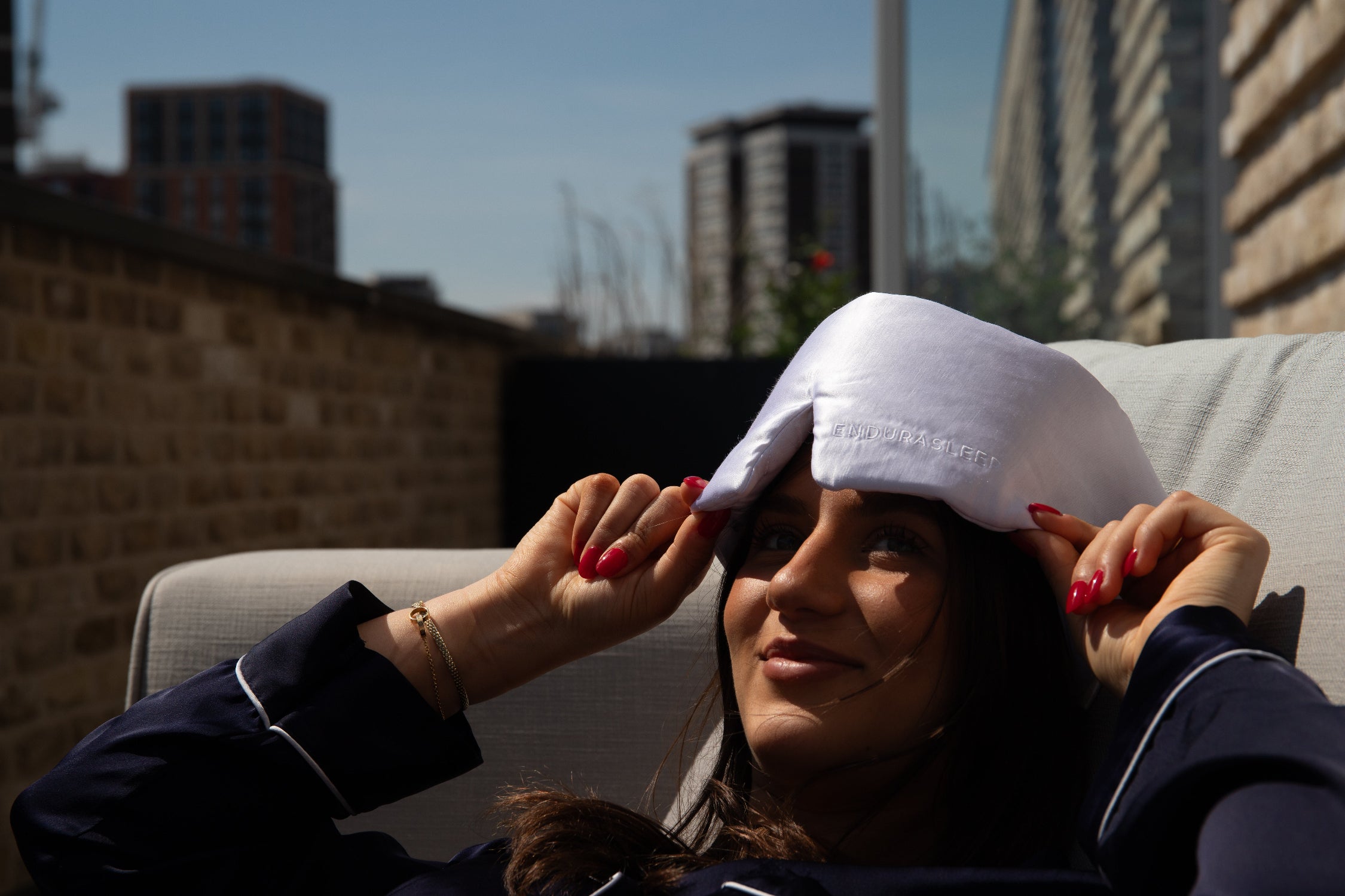 Woman adjusting enduraluxe sleep mask on a rooftop with buildings in the background